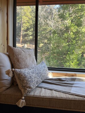 Enjoy a peaceful retreat with a view of the lush forest from the large window, featuring a comfortable bed and natural decor.