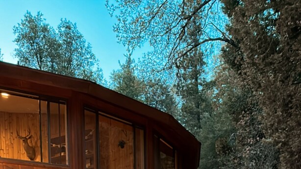 A wooden deck with lounge chairs and a glass table, surrounded by a wooden cabin with a staircase and string lights. - Spacious Secluded Cabin on 9 acres Hot Tub Outdoor Dining Private Trails (Idyllwild-Pine Cove)
