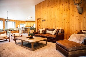 Un salon chaleureux avec un mur en bois, des meubles en cuir et une tête de cerf accrochée au mur.