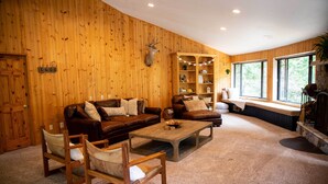 A cozy living room with a wooden wall, a fireplace, and a large window. - Spacious Secluded Cabin on 9 acres Hot Tub Outdoor Dining Private Trails (Idyllwild-Pine Cove)