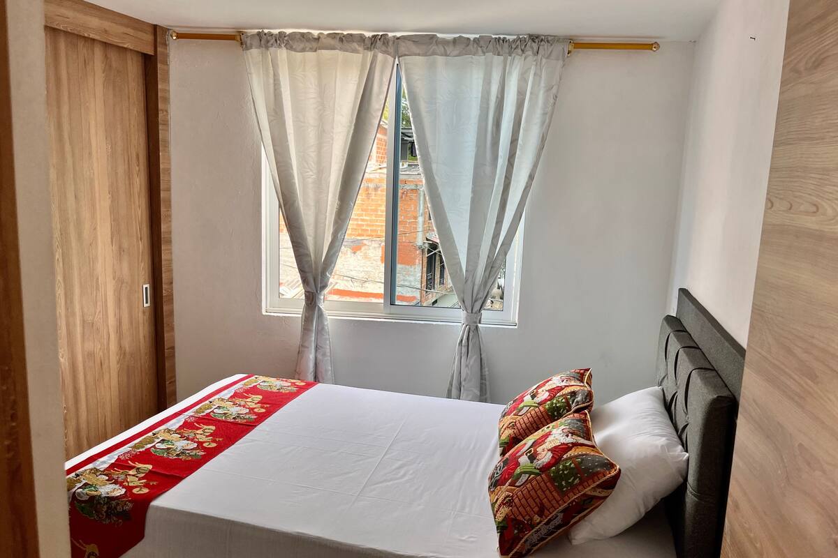 A bed with a red and white bedspread, a patterned pillow, and a window with curtains.