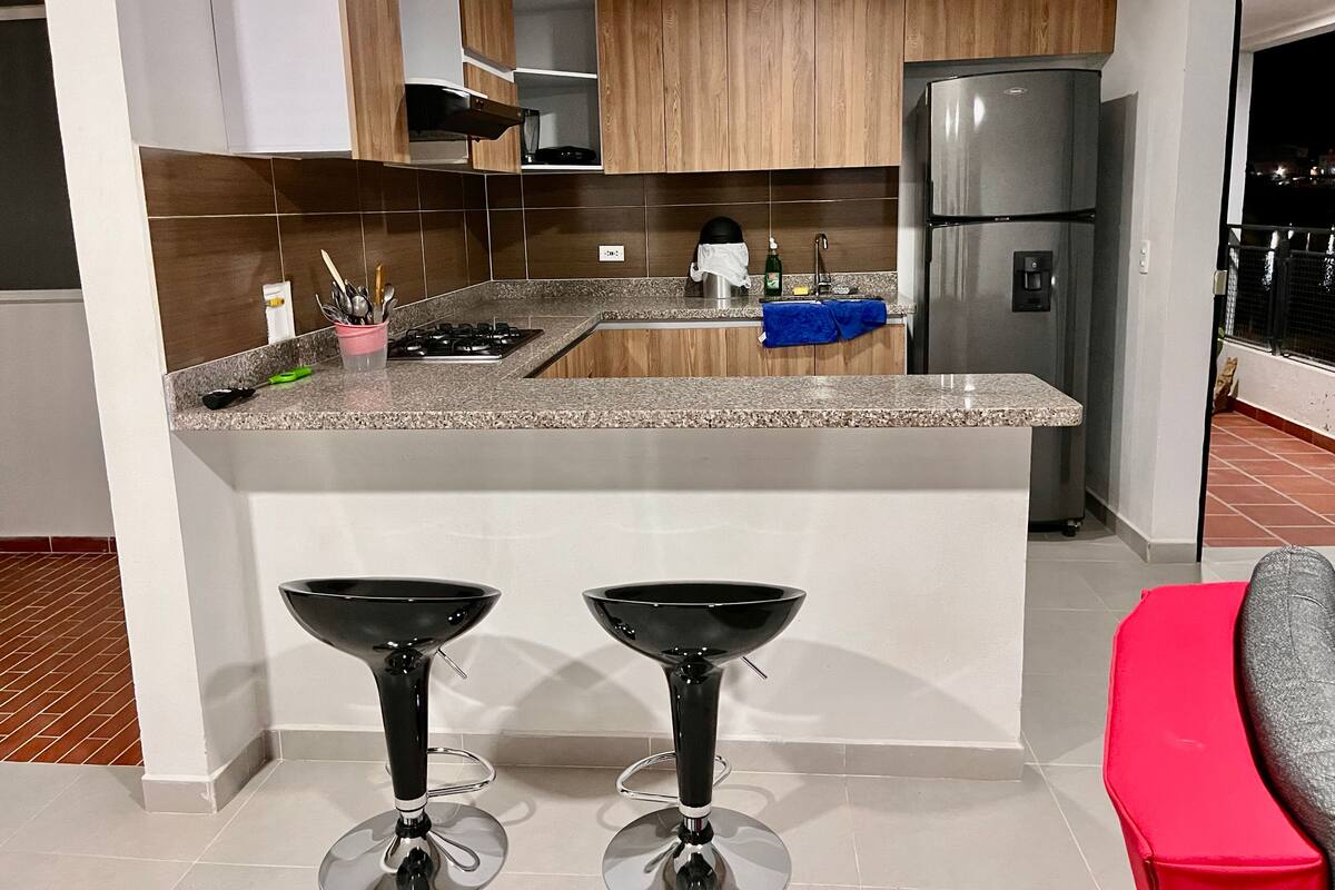 A modern kitchen with a central island, stainless steel appliances, and two bar stools.