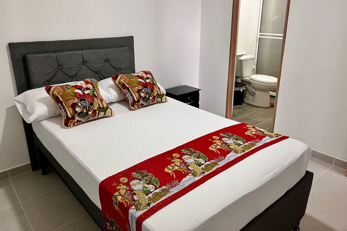 A neatly made bed with a white mattress, two decorative pillows, and a red bedspread with a Christmas theme.