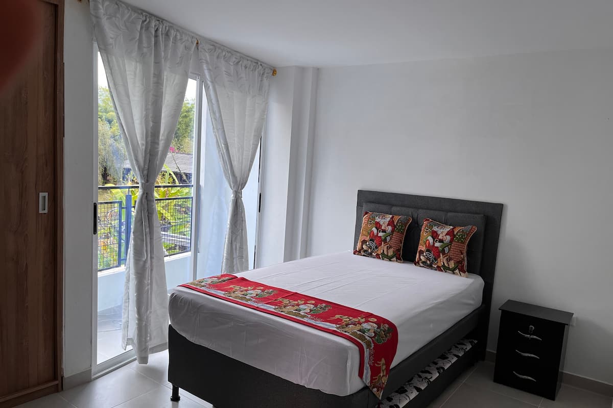 A bedroom with a bed, a nightstand, and a view of the outside.