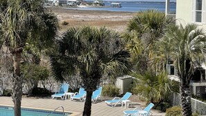 Un espace piscine avec des chaises longues, une voiture blanche et une vue sur la plage et l’océan.