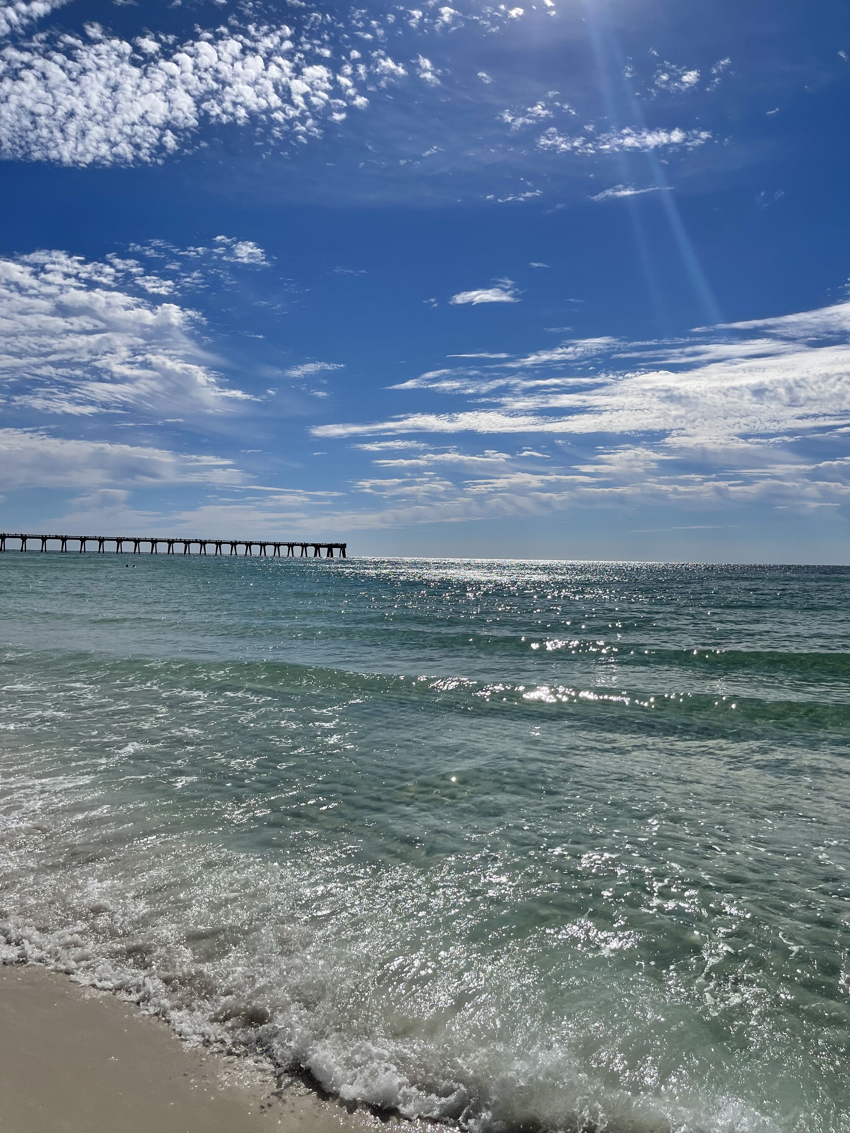 A beach with clear water, waves, and a pier in the distance.