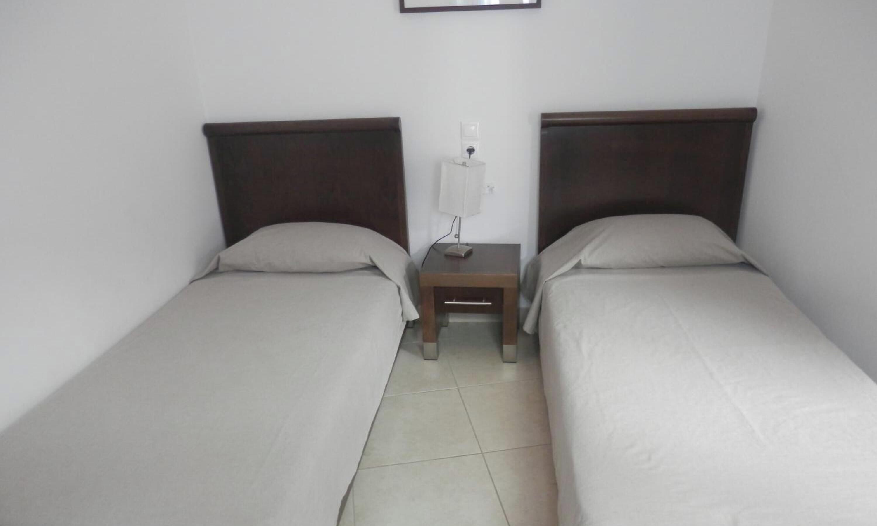 Habitación doble con dos camas individuales, una mesita de noche con lámpara e interruptor de luz en la pared.