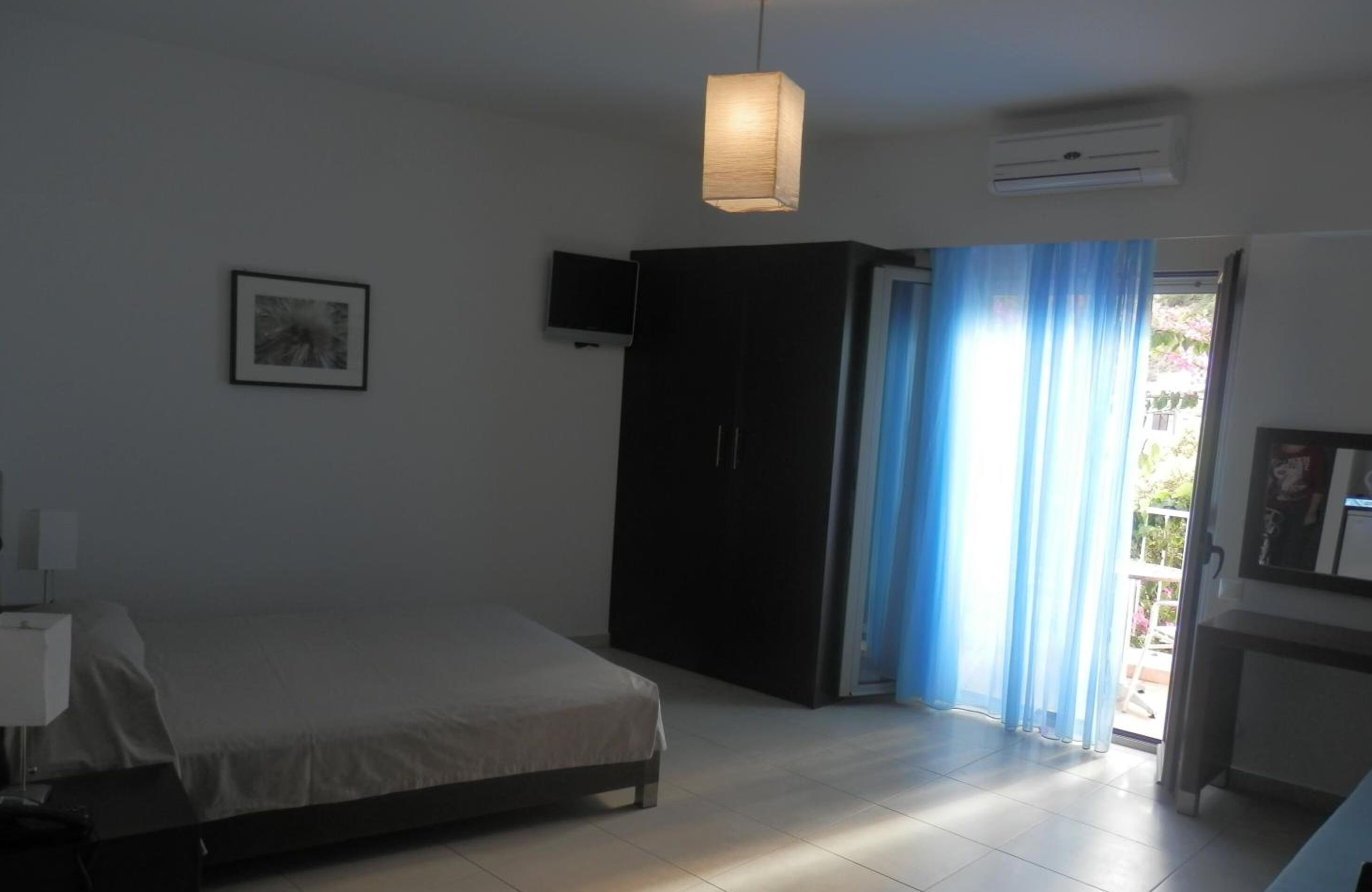 A bedroom with a bed, a wardrobe, a television, and a window with curtains.