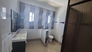 A bathroom with a sink, mirror, toilet, and a window with blinds.