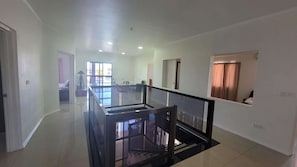 A spacious hallway with a glass railing, leading to a staircase and a room with a view.