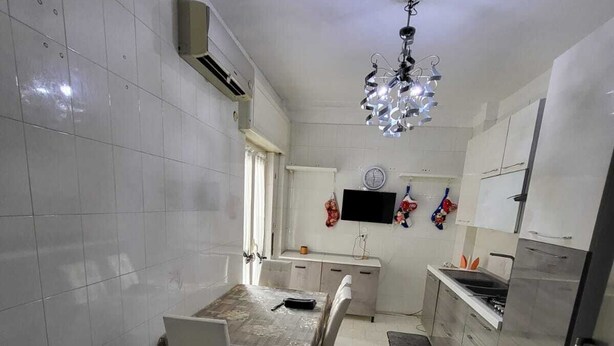 A compact kitchen with white tiled walls, a dining table with chairs, a refrigerator, and a microwave. - Apartment 3 min from the Museum (Napoli)