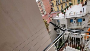 A balcony with a tiled floor, a blue trash bin, a white chair, and a black bag. - Apartment 3 min from the Museum (Napoli)