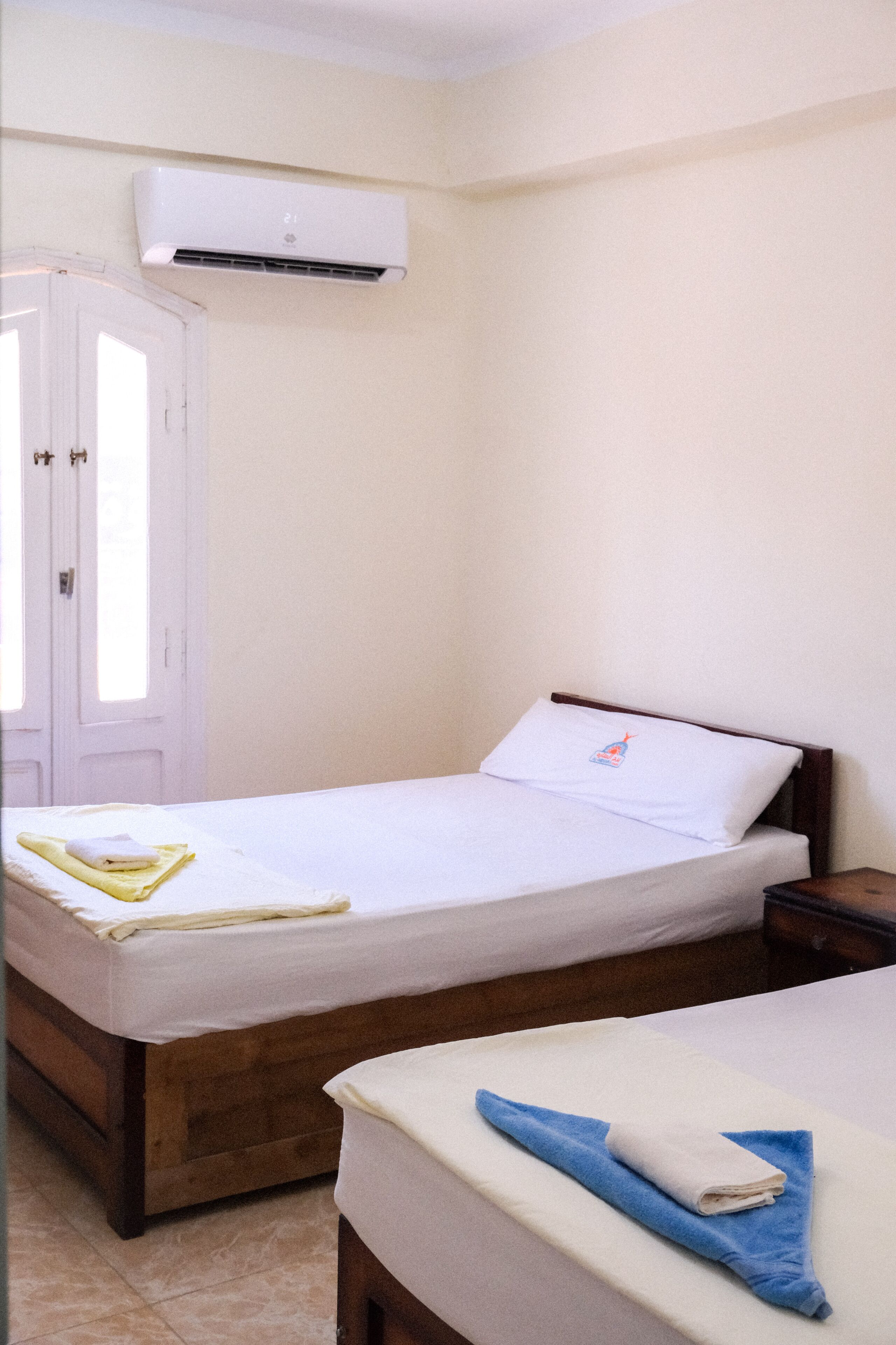 Une chambre d’hôtel avec un lit simple, une table de chevet et un climatiseur fixé au mur.
