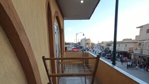 A balcony with two wooden chairs, a metal railing, and a view of a busy street with buildings and vehicles. - Al-Manara Hostel Siwa Oasis (Siwa)