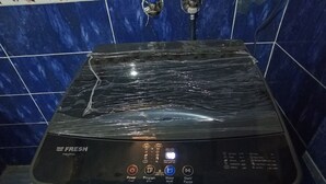 A black washing machine with a control panel, located in a bathroom with blue tiles and a floral border. - Al-Manara Hostel Siwa Oasis (Siwa)