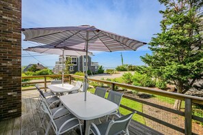 Eine Holzterrasse mit Tisch, Stühlen und Sonnenschirm, mit Blick auf Häuser und Bäume.