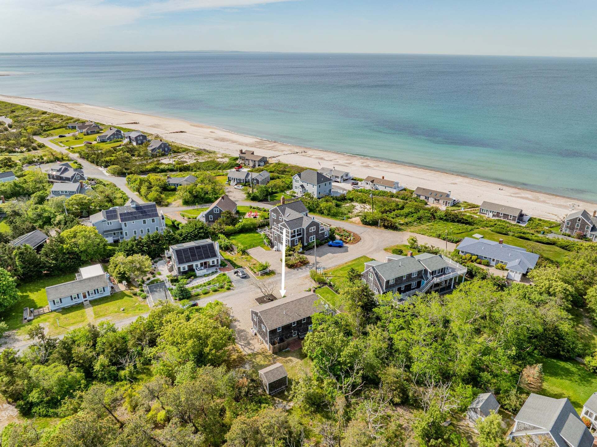 An aerial view of a coastal residential area with houses, a beach, and a clear view of the ocean.