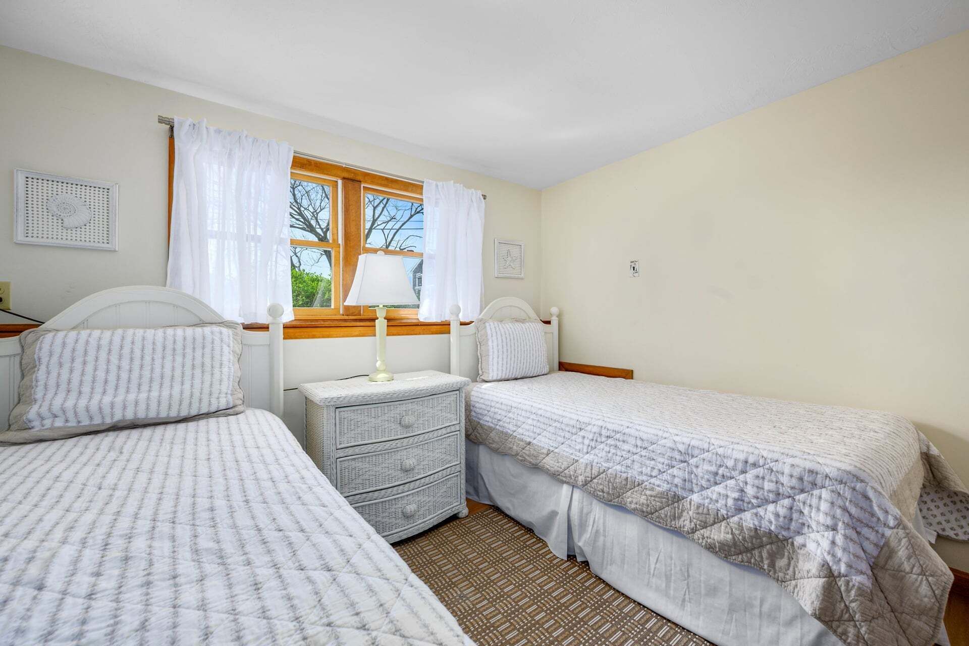 A bedroom with two single beds, a bedside table with a lamp, a small dresser, and a window with curtains.