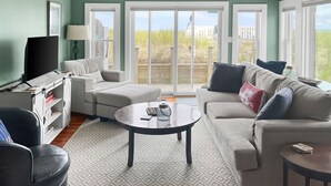 A living room with a large window, a television, a sofa, and a coffee table. - Cozy Sagamore Beach Cottage w/ Modern Comforts (Sagamore Beach)