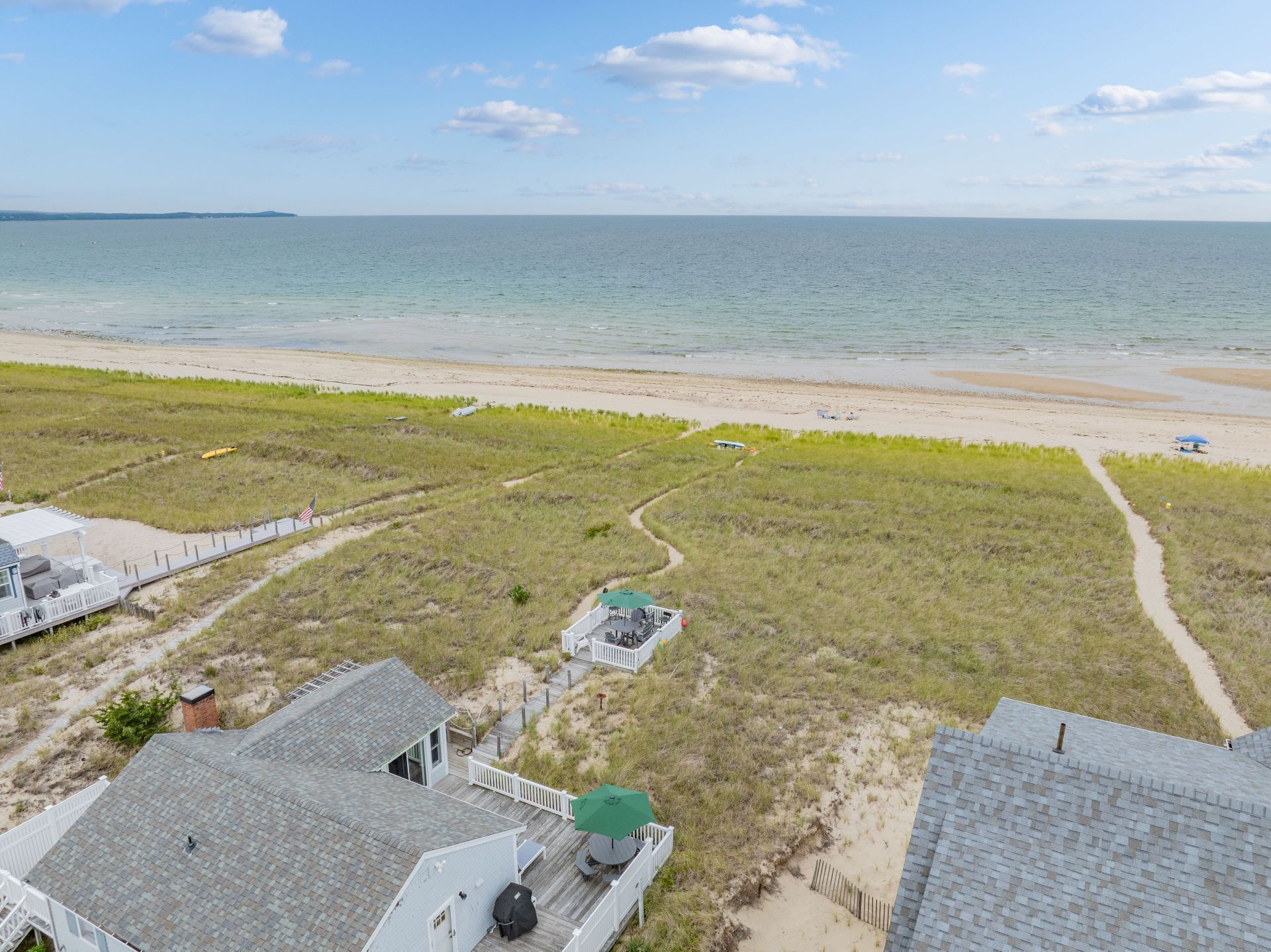 Une propriété située en bord de mer, dotée d’une plage de sable, d’une terrasse en bois et offrant une vue sur l’océan.