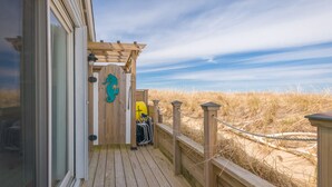 A wooden deck with a glass door leading to a room, a wooden pergola with a starfish decoration, and beach chairs on the deck. - Cozy Sagamore Beach Cottage w/ Modern Comforts (Sagamore Beach)