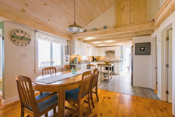 A wooden dining table with chairs, a clock, and a window with curtains.