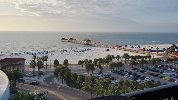Una playa con un muelle, palmeras y un aparcamiento.