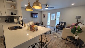 Una cocina moderna con una isla grande, luces colgantes y un comedor con sofá y mesa de centro.