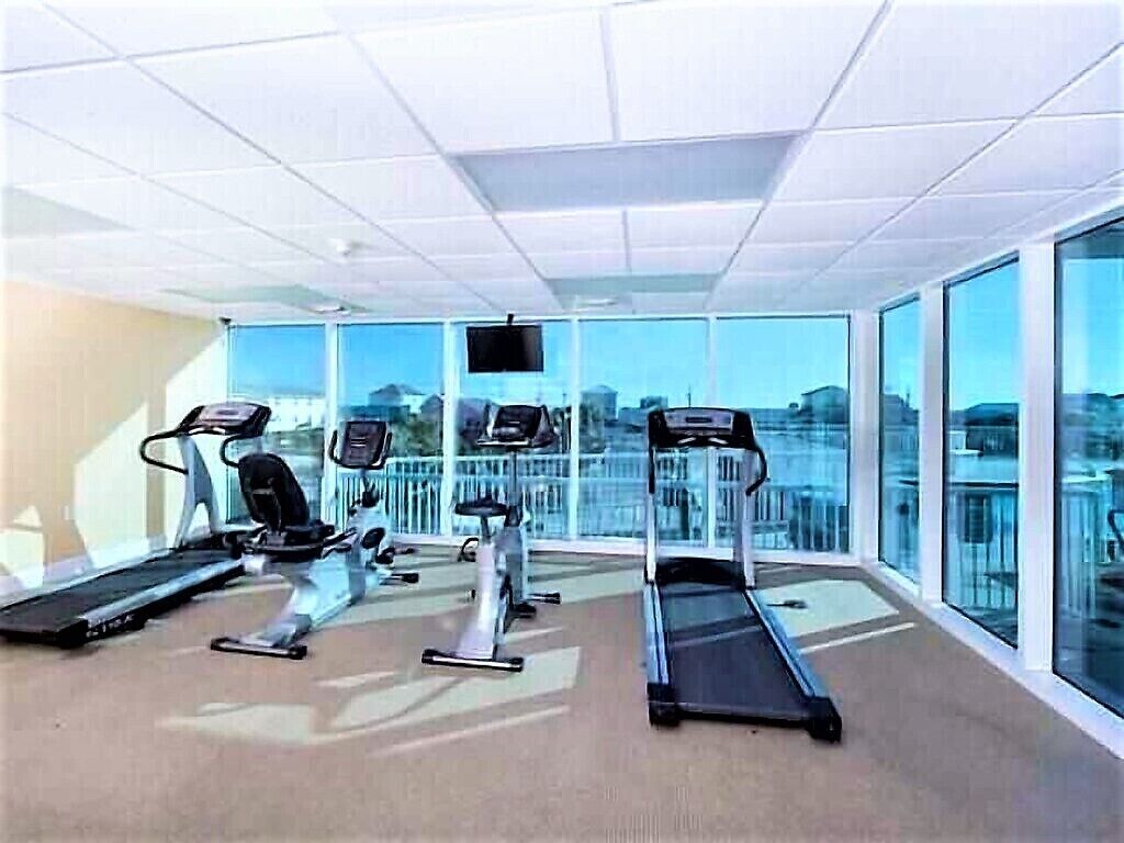 Un gimnasio con cintas de correr, bicicletas estáticas y una máquina de remo, ventanas amplias con vista a la ciudad.