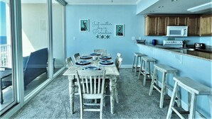 A dining area with a table set for four, a ceiling fan, and a kitchen area with a microwave. - Welcome to our Beach Dream View, The Sunrise and Sunset are breath taking (Gulf Shores)