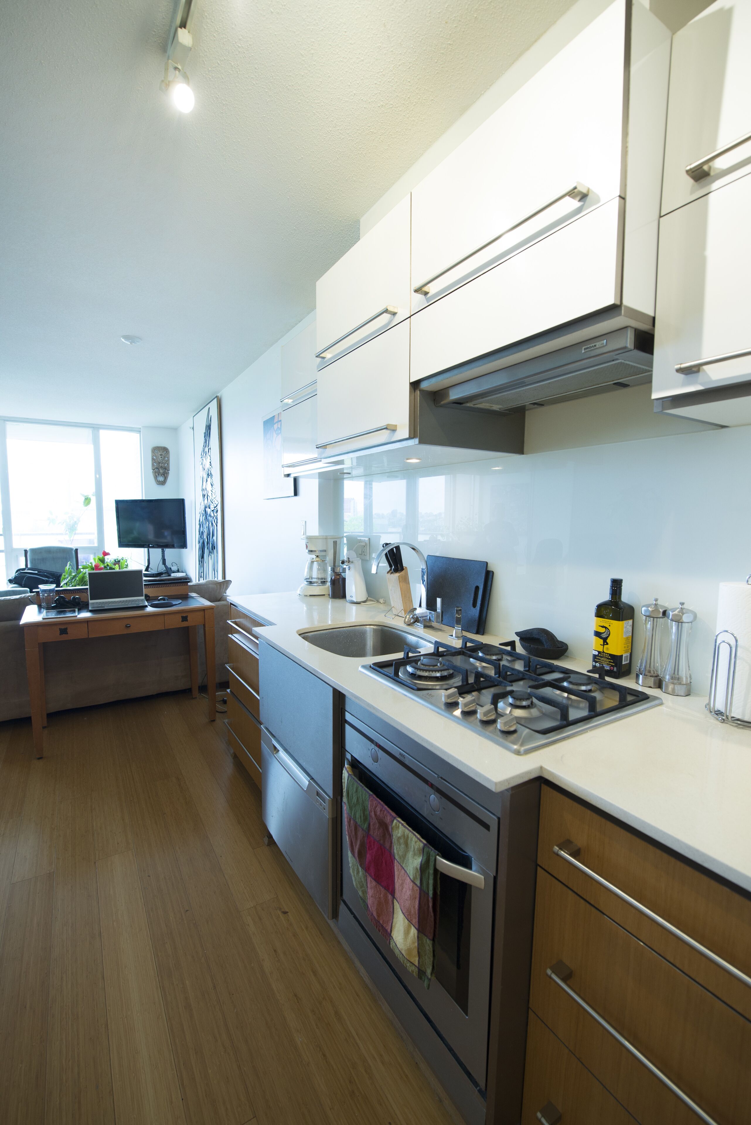 A modern kitchen with a gas stove, oven, and a dining area with a laptop and a coffee maker.