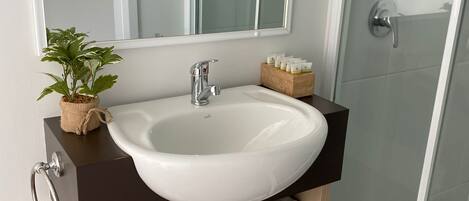 A bathroom with a white sink, a mirror, a potted plant, and a towel rack.