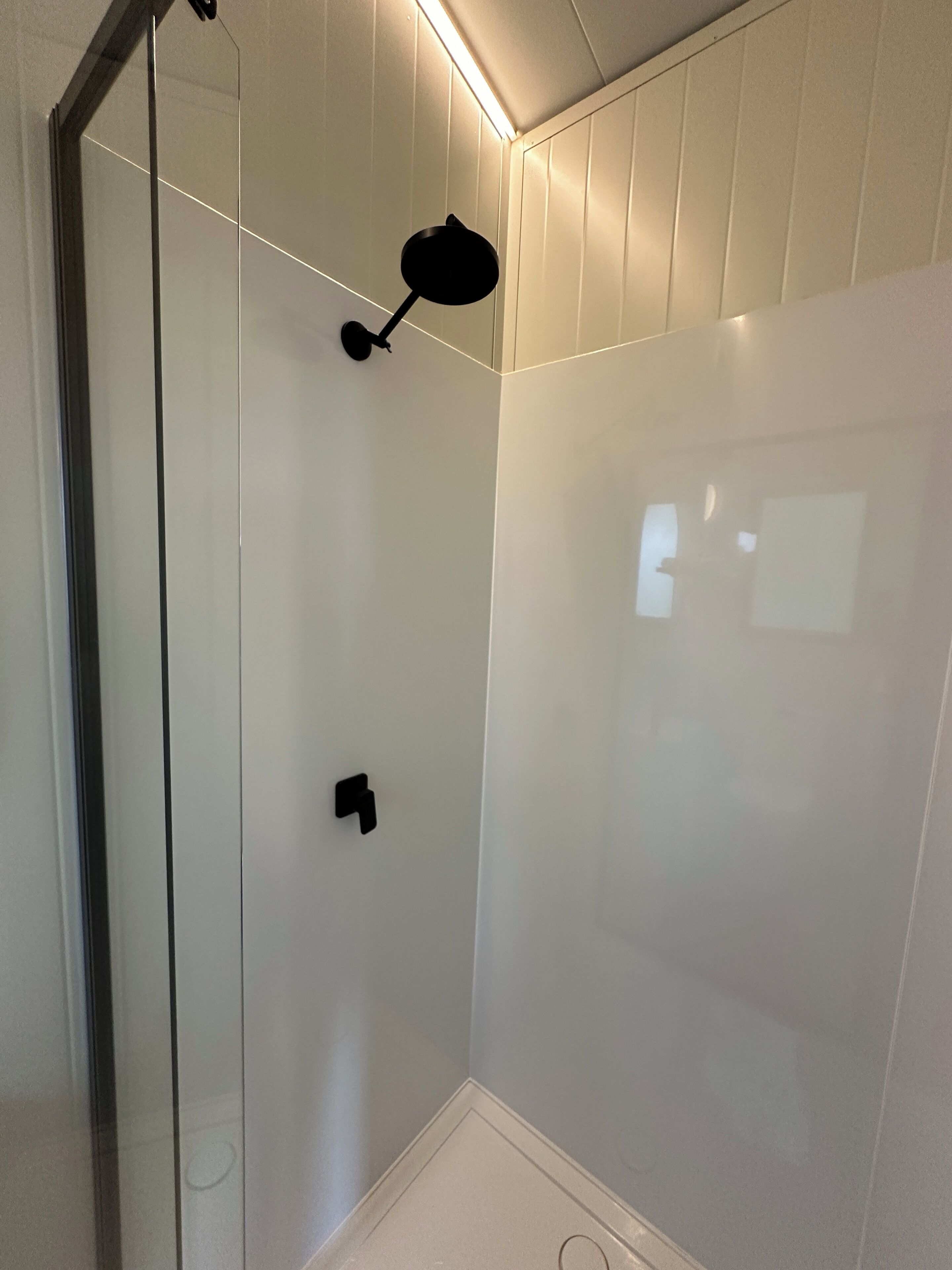 Une salle de bain moderne avec une douche à parois de verre, un luminaire noir fixé au mur et un mur recouvert de carreaux blancs.
