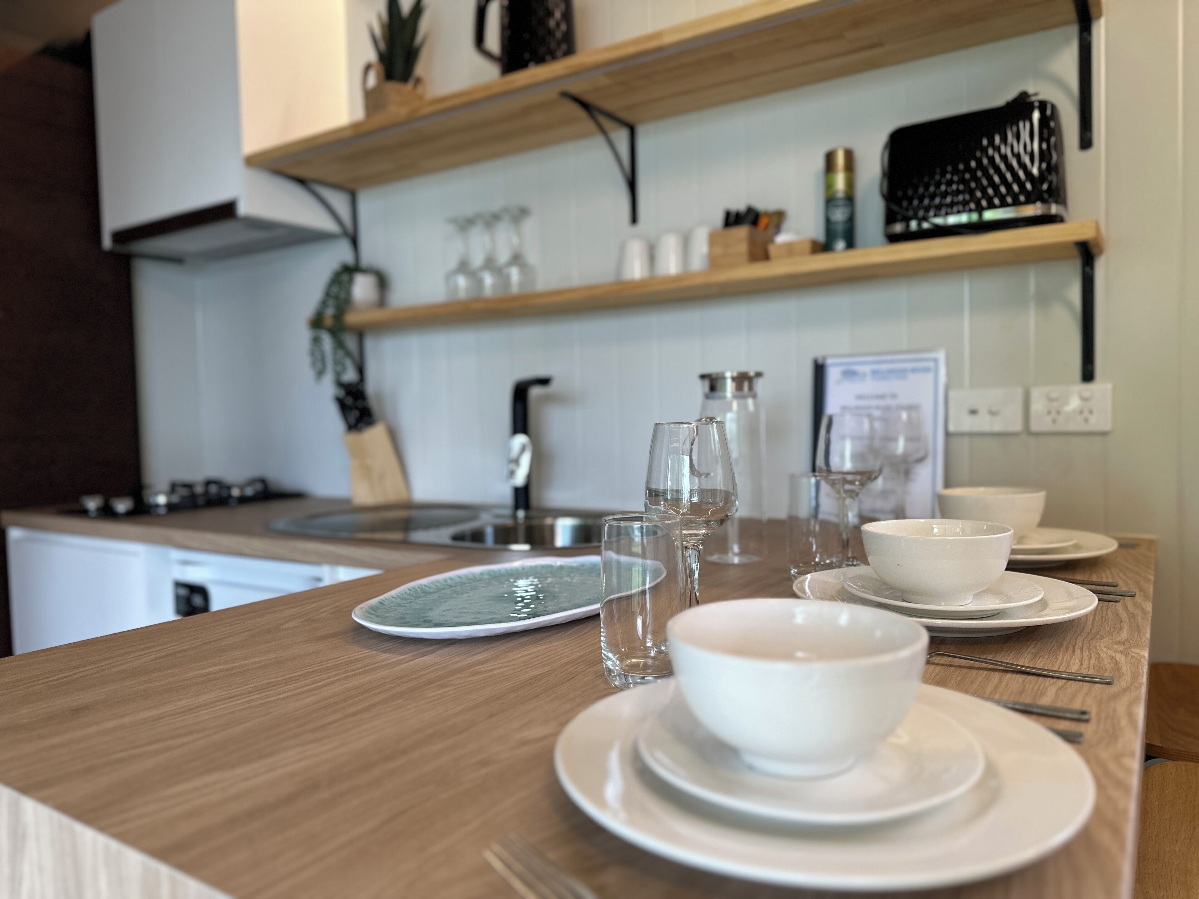 En køkkenbordplade i træ, en vask og forskellige køkkenartikler, herunder drikkeglas og en kaffemaskine.