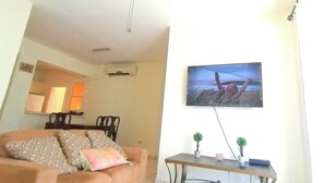 Un soggiorno con divano, tavolino, televisione a parete e ventilatore a soffitto.