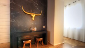 A modern interior with a black marble wall, a golden bull head decoration, a black fireplace, and two wooden stools. - Luxury Living in the Heart of the City (Cagliari)