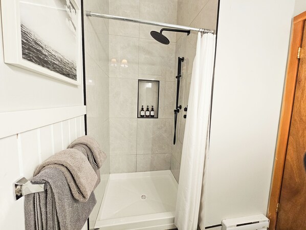 Un espace douche moderne avec une porte en verre, une baignoire blanche et un porte-serviettes sur lequel est posée une serviette pliée.