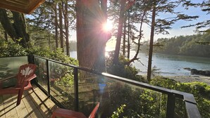 Una terraza de madera con sillas rojas, con vista a un bosque y una masa de agua.