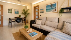 A modern living room with a sofa, coffee table, dining table, chairs, and wall art. - Josep Folch – Center, Parking & A/C Tossa (Tossa De Mar)