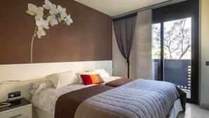 A modern bedroom with a large bed, a nightstand, and a window with a view of trees. - Josep Folch – Center, Parking & A/C Tossa (Tossa De Mar)