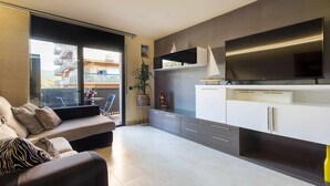 A modern apartment with a balcony, a sofa, a TV, and a kitchen area. - Josep Folch – Center, Parking & A/C Tossa (Tossa De Mar)
