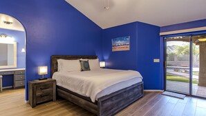 A bedroom with a bed, bedside tables, a dresser, a large window, and a view of the outdoors. - Mountain Home Pool VIEWS Garage FUN Backyard Spacious Private Close to UofA
 (Tucson)