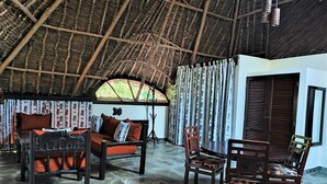 A room with a thatched roof, stone flooring, a sofa, chairs, and curtains.