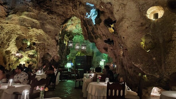 An underground restaurant with tables and chairs arranged in a cave-like setting, illuminated by hanging lanterns.