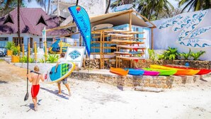 A beachside building with a sign for 'The Crab' restaurant, a wooden structure with surfboards, and a wall with water sports text.