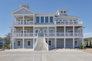 Una casa frente al mar de dos pisos con una escalera central, balcones y un porche cubierto.