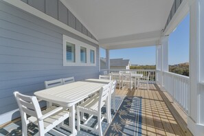 Un espacio al aire libre techado con un deck de madera, mobiliario blanco y vistas al paisaje.