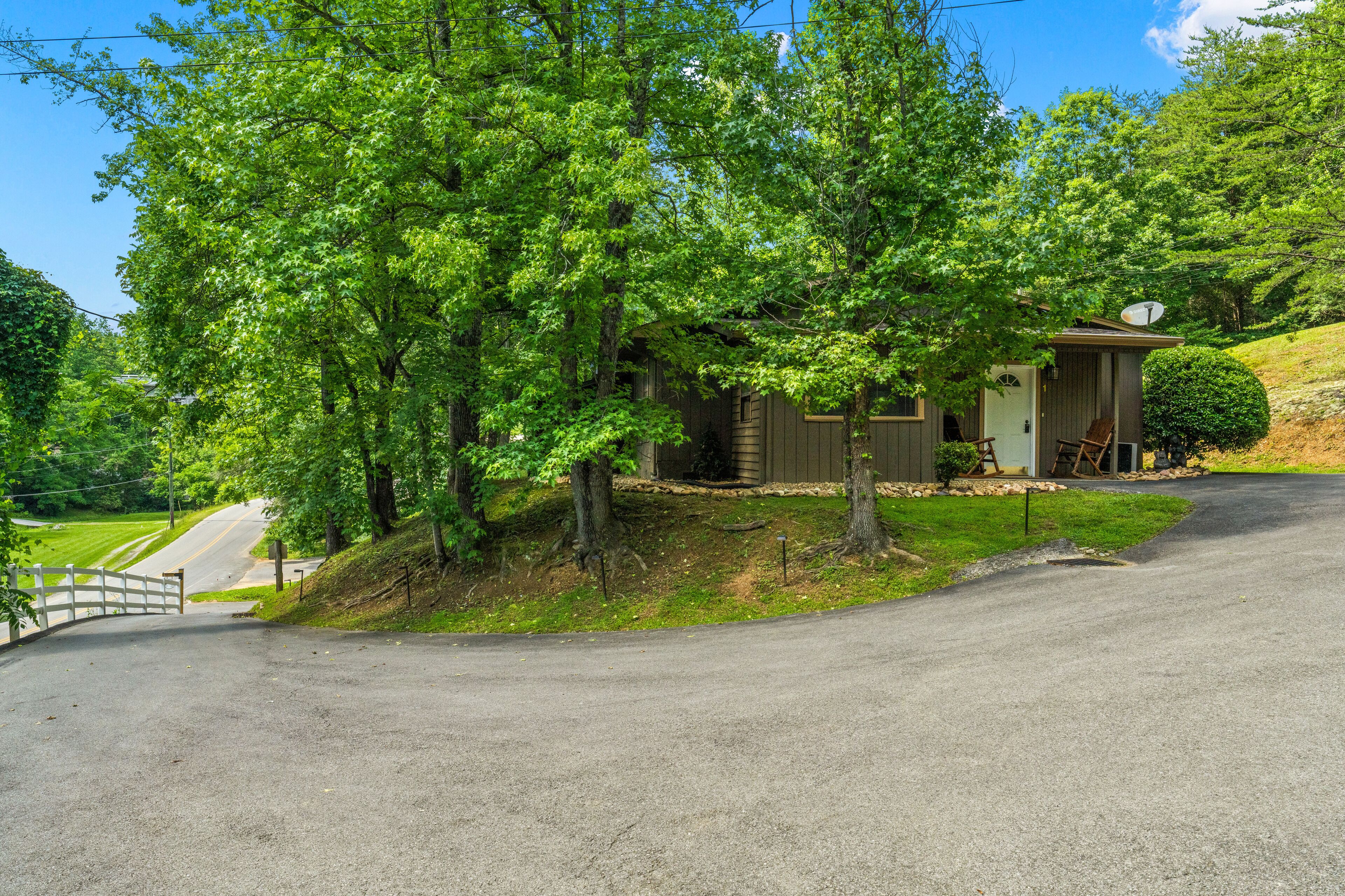 A small house with a porch, surrounded by trees and a road.