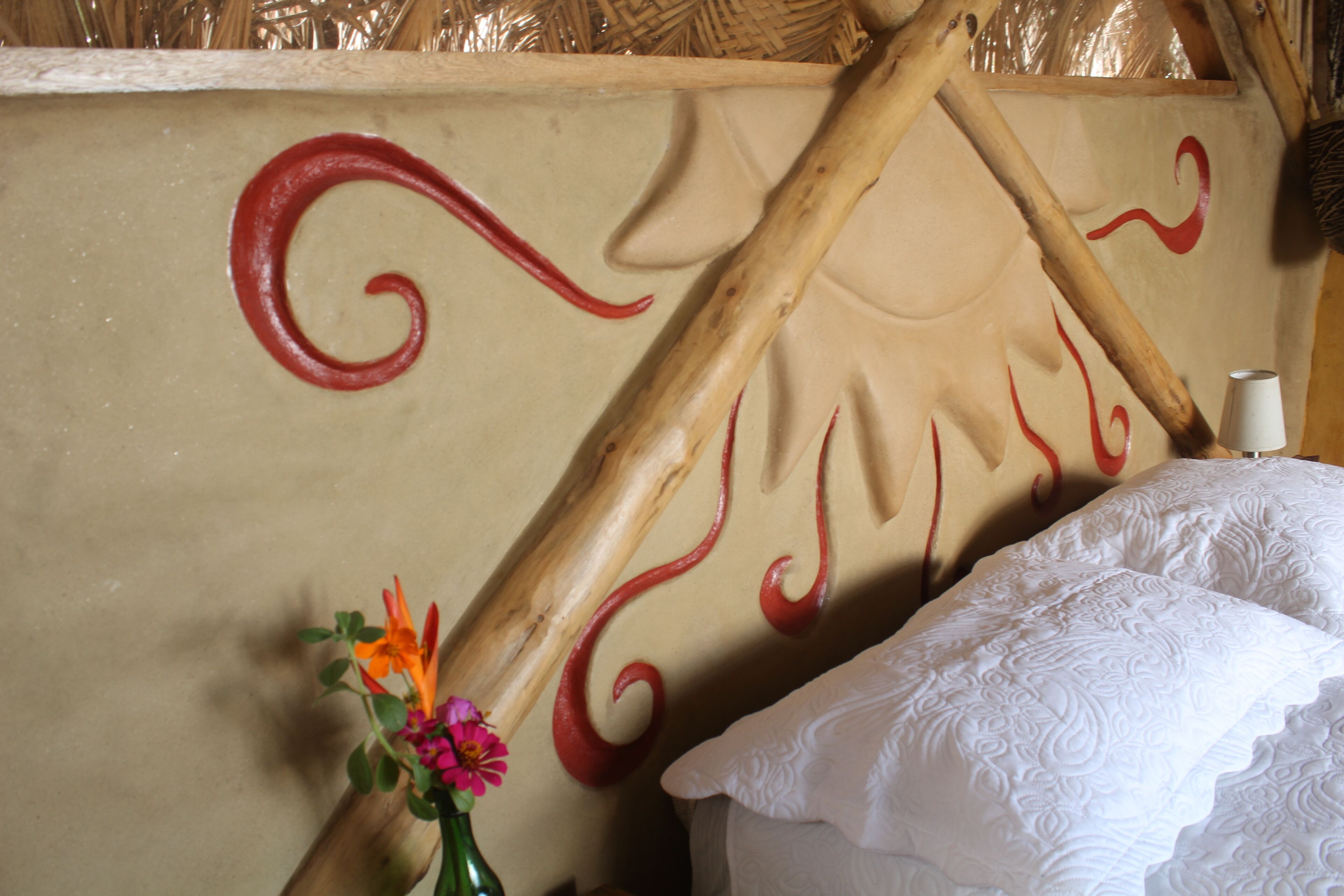 Een kamer met een bed, een vaas met bloemen en een muur met rode decoratieve patronen.