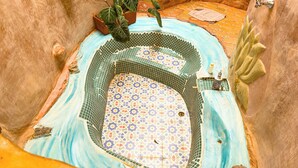 Uma pequena banheira de hidromassagem com azulejos, borda decorativa e uma planta no canto.